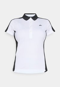 Πολο πουκάμισο σε λευκό με μαύρες λεπτομέρειες, με γιακά, πατιλέτα με τρία κουμπιά και κοντά μανίκια. Κατασκευασμένο από λείο, ελαφρύ ύφασμα.