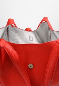 Punainen nahkainen olkalaukku, jossa on kuvioitu pinta, hopeinen sisävuori, kaksi kantohihnaa ja magneettisuljin.