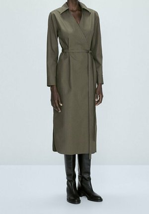 Olive green wrap dress with long sleeves, a collar, and a tie waist detail. Worn with sleek black knee-high boots. Smooth fabric texture.