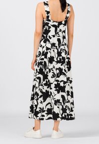 Kwiatowa sukienka midi z czarno-białym wzorem, kwadratowym tyłem i szerokimi ramiączkami. Do tego białe trampki na neutralnym tle.