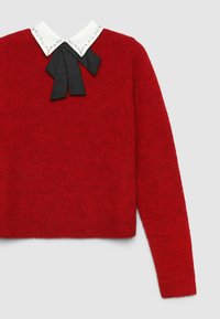 Roter Strickpullover mit einem weißen Kragen, der mit Strasssteinen besetzt ist, und einem schwarzen Fliegenknoten in der Mitte. Lange Ärmel, gerippter Saum.
