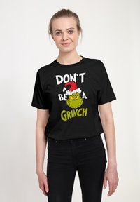 Czarny t-shirt z krótkim rękawem z grafiką Grincha w czerwonej czapce Mikołaja oraz białym i zielonym napisem: „NIE BĄDŹ GRINCHEM.”