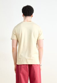 Beige t-paita lyhyillä hihoilla ja pyöreällä kaula-aukolla, jossa on sileä pinta ja rento istuvuus, yhdistettynä löysiin vaaleanpunaisiin housuihin.