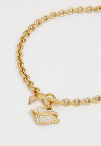 Gouden schakeltjesarmband met een sluiting in de vorm van een toggle en een hartvormige hanger versierd met heldere rhinestones. Kleine merklabel bevestigd.