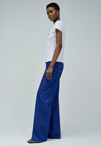 Camiseta blanca de algodón combinada con jeans de denim azul de pierna ancha. Los jeans presentan costuras visibles y un detalle en el bolsillo trasero.