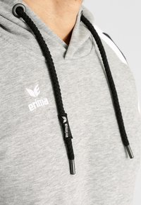 Felpa grigia con cappuccio caratterizzata da un laccio nero, texture a costine e un logo bianco sul petto. Finiture nere accentuano la felpa.