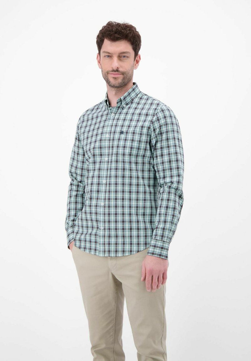 Zielono-niebieska koszula w kratę na guziki, z długimi rękawami i kołnierzykiem. Tekstura materiału jest gładka. Noszona z jasnymi spodniami.