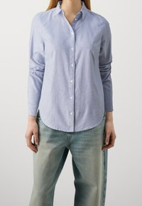 Blå och vit randig skjorta med knappar och långa ärmar, krage, rund nederkant och textil i bomull. Bärs med ljusblå jeans.