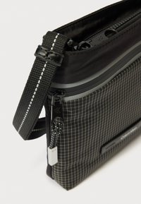 Fekete keresztpántos táska kockás első zsebbel, márkás cipzárhúzókkal és fehér varrással díszített állítható pánttal.