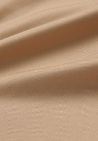 Tissu beige avec une texture nervurée, présentant des plis doux et une surface lisse. La lumière se reflète subtilement, mettant en valeur son éclat et sa richesse.