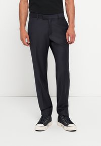 Calças sob medida cinza escuras com frente lisa, passadores de cinto e uma textura suave, combinadas com ténis pretos de cano alto e uma blusa preta.