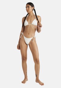Set bikini bianco con coppa triangolare e slip laterale annodato, decorato con un delicato motivo floreale, realizzato in tessuto morbido ed elastico.