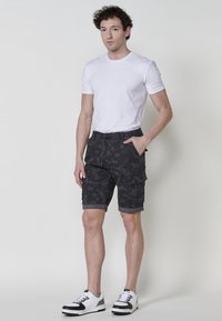 Shorts cargo noirs avec un motif texturé, dotés de poches latérales et de revers roulés, assortis à un t-shirt blanc uni et des baskets blanches.