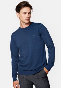 Granatowy sweter z okrągłym dekoltem, wykonany z miękkiego materiału, z długimi rękawami i prążkowanym pasem w talii. Subtelny detal logo na piersi.