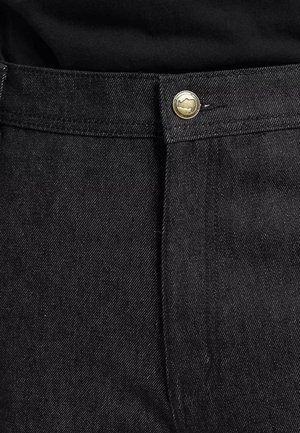 Jean en denim noir avec une coupe droite, une fermeture à bouton en laiton et une texture subtile. Détails de couture le long de la taille.