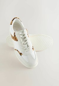 White leather sneakers featuring a leopard print accent, textured design, flat laces, and a patterned rubber sole.