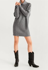 Graues gestricktes Sweatkleid mit einem Rollkragen, langen Ärmeln und schmalem Schnitt, kombiniert mit schwarzen Cowboy-Stiefeln mit spitzer Zehe und Absatzsohle.