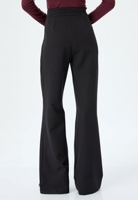 Zwarte wijde broek met een hoge tailleband, gladde stof en plooien aan de voorkant. Het ontwerp is op maat gemaakt en benadrukt een strakke silhouette.