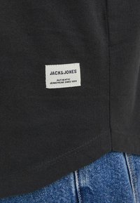 Czarna bawełniana koszulka z małą białą metką z napisem "JACK & JONES" oraz szczegółami, w połączeniu z niebieskimi dżinsami.
