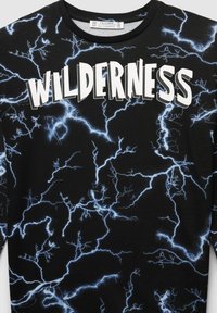 T-shirt nera con un motivo a saetta e la parola "WILDERNESS" in grassetto bianco sulla parte anteriore.