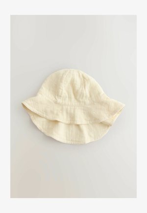 Világos krémszínű pamut vödörkalap texturált pöttyös mintával, széles, lelógó karimával és puha, laza formával.