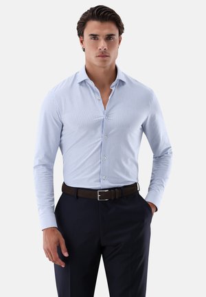 Hellblau gestreifte Hemdbluse mit Button-Down-Kragen, langen Ärmeln und slim fit, kombiniert mit dunklen Hosen und einem braunen Gürtel.