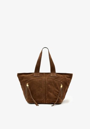 Sac cabas en daim marron avec deux poignées supérieures, poches avant zippées avec pompons, et une forme souple et décontractée.