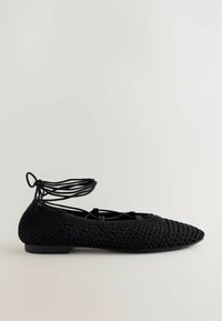 Svarta vävda ballerinaskor med spetsig tå och en tunn ankelrem. Har en texturerad ovandel och en låg, solid svart klack.