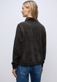 Donkerbruin ribfluwelen jack met een hoge kraag, ribbelmanchetten en zoom. Draag het met lichtblauwe jeans met een gestructureerd oppervlak.