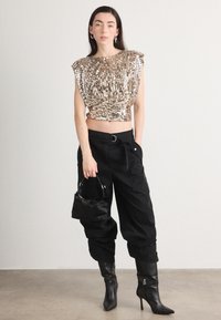 Un top fără mâneci, cu paiete aurii și un design bufant, asortat cu pantaloni negri largi și cizme cu toc înalt negre. O geantă mică neagră completează ținuta.