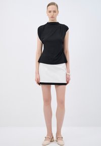 Top nero con maniche corte e collo alto, abbinato a una mini gonna bianca con orlo nero. Modella che indossa scarpe beige con plateau.