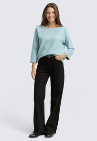 Lichtblauw longsleeve top met een brede halslijn, gecombineerd met zwarte broek met hoge taille en zwarte schoenen. Gladde stof en een ontspannen pasvorm.