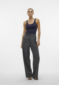 Canottiera blu navy abbinata a pantaloni grigi a gamba larga con vita alta, caratterizzati da pieghe, una texture liscia e un design minimalista. Sandali neri completano l'ensemble.