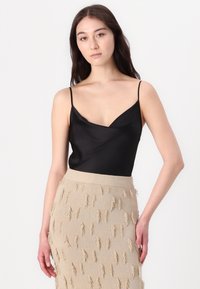 Schwarzes Satin-Camisole mit schmalen Trägern und V-Ausschnitt. Kombiniert mit einem beigen Strickrock, der mit strukturiertem Fransenbesatz verziert ist.