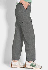 Grau karierte Hose mit lockerer Passform, seitlichen Taschen und Druckknopfakzenten. Kombiniert mit weißen Sneakers mit grünen Details.