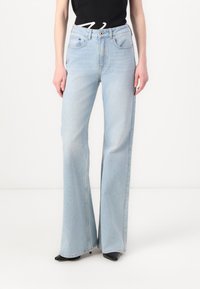 Lyseblå vidbukse i denim med frontlommer, knappelukking og en lett falmet tekstur. Kombinert med svarte sko.