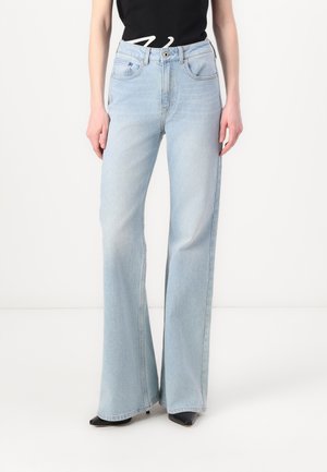 Jeans de pierna ancha azul claro de denim, con bolsillos frontales, cierre de botón y una textura ligeramente desgastada. Combinados con zapatos negros.