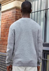Suéter de punto gris con cuello redondo, puños y dobladillo acanalados, que presenta una textura suave y un ajuste casual. Adecuado para conjuntos en capas.