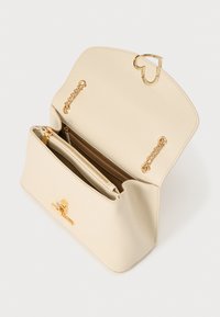 Τσάντα χειρός από δέρμα σε μπεζ χρώμα με χρυσό κούμπωμα σε σχήμα καρδιάς. Στο εσωτερικό διαθέτει τσέπη με φερμουάρ και διακοσμητικές αλυσίδες σε χρυσό χρώμα. Ομαλή υφή, με σταθερό σχήμα.