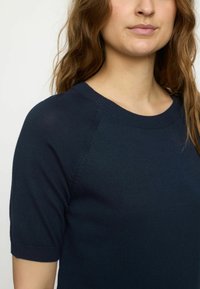 Haut en tricot à manches courtes bleu marine, avec un col rond côtelé et une texture lisse, conçu avec des manches raglan pour plus de confort.