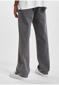 Jeans de mezclilla gris holgados con una textura desgastada, que presentan dos bolsillos traseros y piernas rectas, combinados con zapatillas blancas.