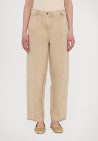 Beige wide-leg trousers with a textured fabric, featuring a high waist, front pockets, and frayed hems, paired with woven gold slip-on shoes.