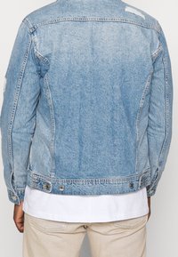 Světle modrá džínová bunda s mírně vybledlým vzhledem, zapínáním na knoflíky, kapsami v bočních švech a opotřebovanými detaily na zádech.