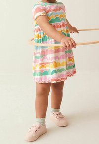 Robe colorée avec un motif festonné en rose, vert, jaune et bleu, dotée de manches courtes et d'un ourlet volé. Baskets roses avec des brides en Velcro.