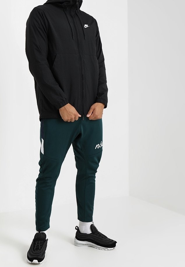 Svart lättviktsjacka från Nike med huva, dragkedjestängning och framfickor. Kombinerad med gröna smala joggers som har en vit logotyp och detaljer.