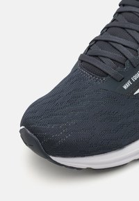 Donkere marineblauwe hardloopschoen met een gestructureerde gebreide bovenkant, opvallende mesh-details en een witte, gevoerde zool. Veters zijn stevig vastgemaakt.