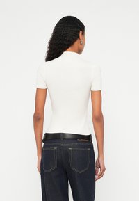 Λευκό ριμπ μπλουζάκι με κοντά μανίκια και ψηλό γιακά, συνδυασμένο με σκούρο τζιν παντελόνι που διαθέτει μαύρη ζώνη και ορατές πίσω τσέπες.