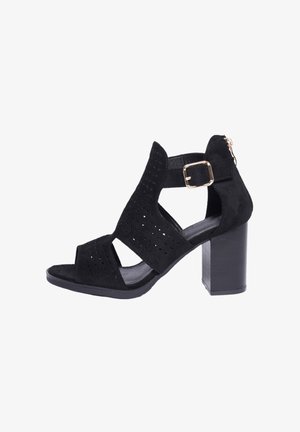 Sandalo alto in suede nero con design perforato. Punta aperta e cinturino alla caviglia con fibbia dorata. Tacco a blocco e interno liscio.