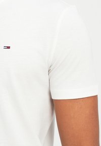 Λευκό βαμβακερό T-shirt με κοντά μανίκια και μικρό κεντητό λογότυπο σε σκούρο μπλε και κόκκινο στο αριστερό στήθος. Λείος υφασμάτινος υφής, λαιμόκοψη σε στυλ crew.