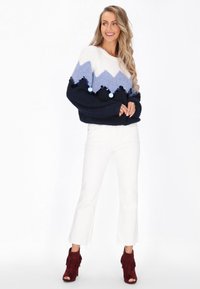 Sweter dziewiarski z wzorem w zygzaki w białym, jasnoniebieskim i granatowym kolorze, z pomponami; w połączeniu z białymi dzwonami i czerwonymi botkami z frędzlami.